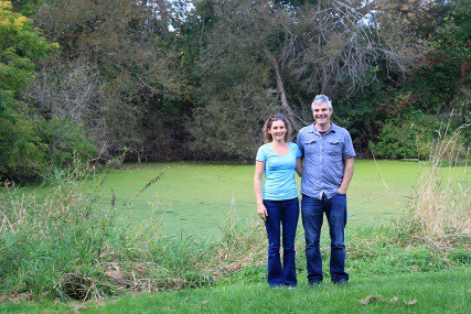 Two landowners pose in front of a pond on their property