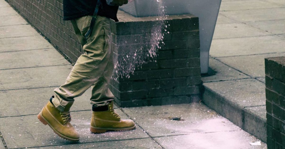 Person sprinkling salt on sidewalk steps