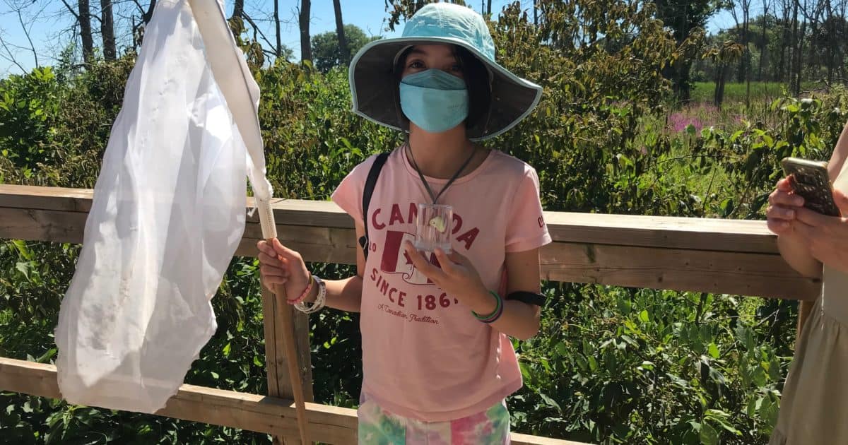 Child wearing mask, holding butterfly net